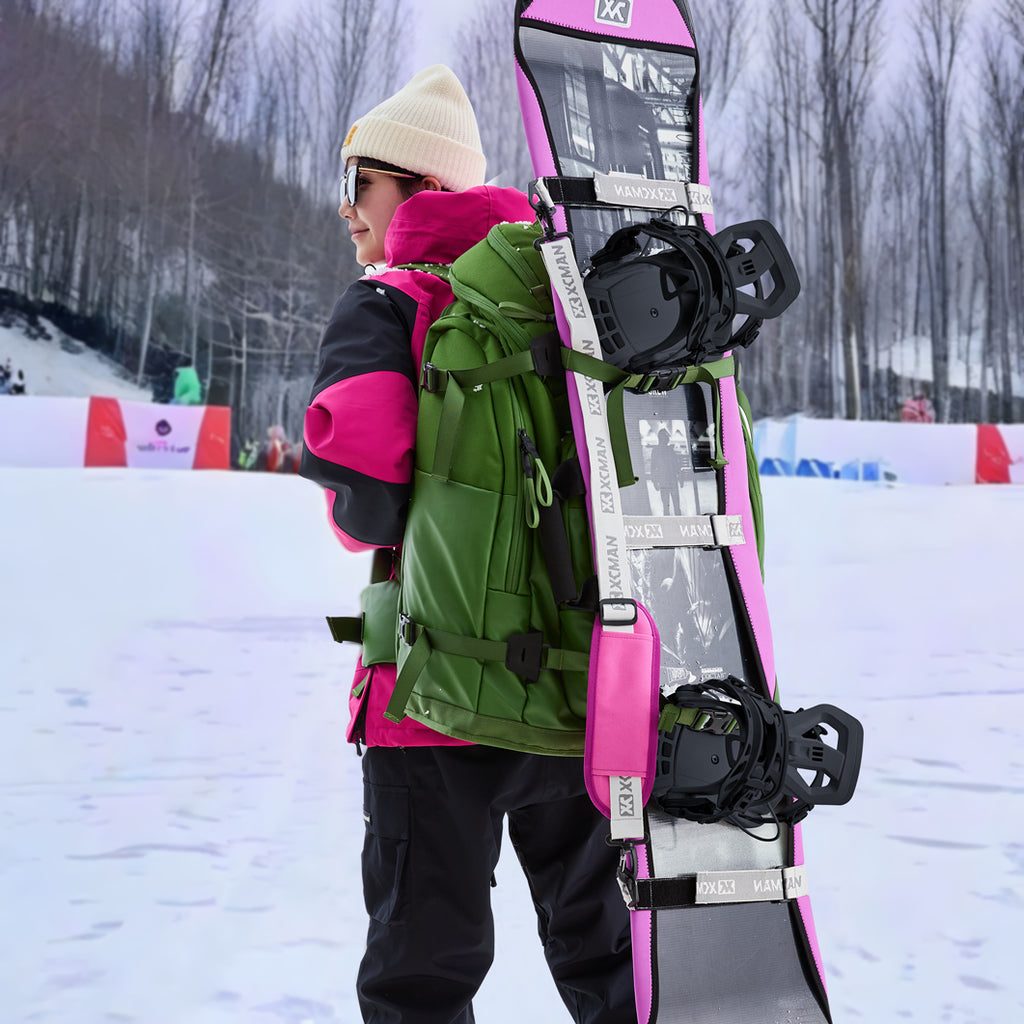 A snowboarder carrying a snowboard equipped with XCMAN 360 Seco bindings in a snowy mountain resort setting