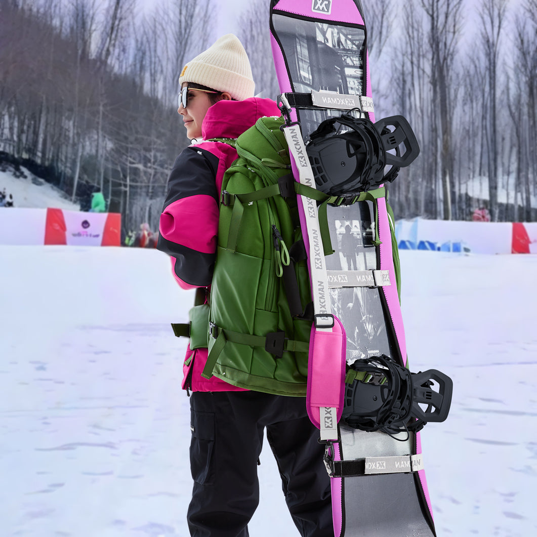 A snowboarder carrying a snowboard equipped with XCMAN 360 Seco bindings in a snowy mountain resort setting