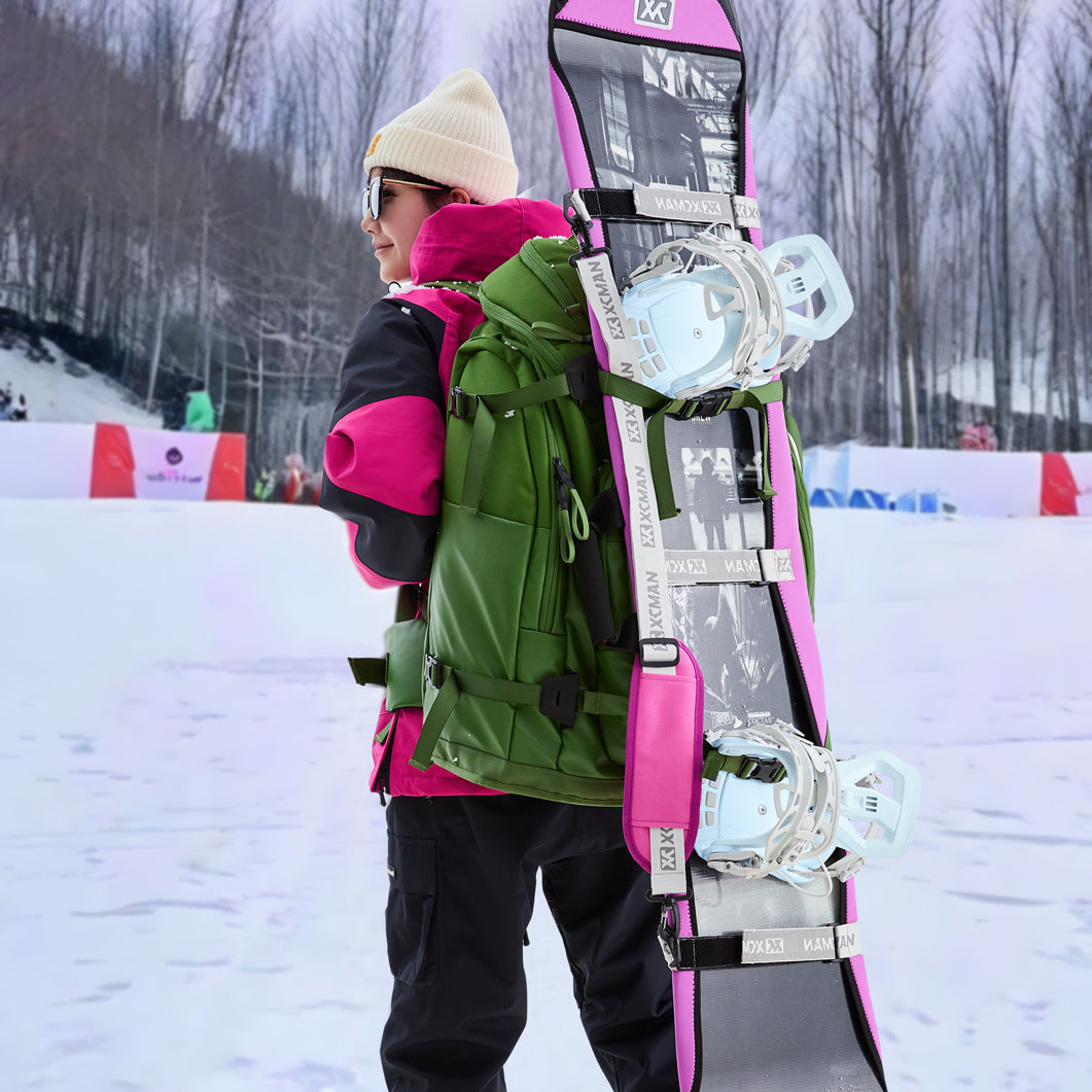 A snowboarder carrying a snowboard equipped with XCMAN 360 Seco white and blue bindings in a snowy mountain resort setting