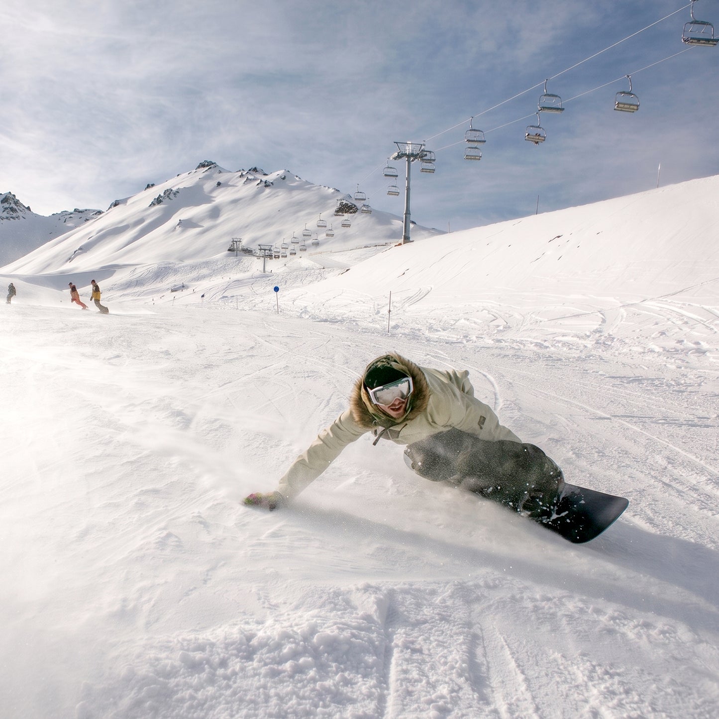 Lifestyle action photo of a snowboarder carving on the XCMAN Men's Black WFB Carving Snowboard down a snowy mountain slope under a blue sky